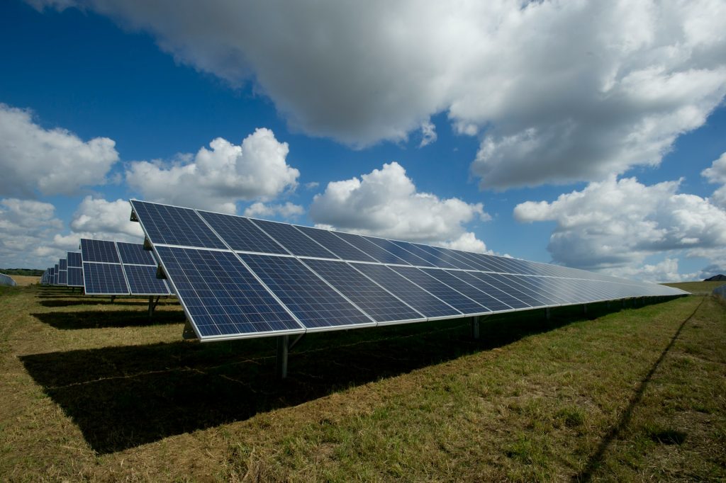 Field of solar panels stretching into the distance under a blue sky with white clouds.