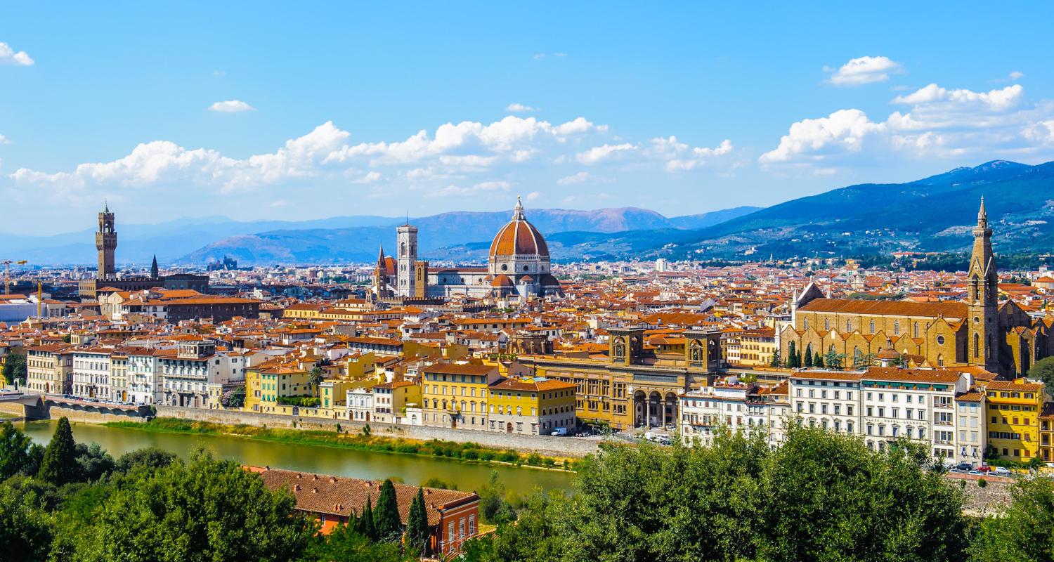A panoramic view of the Florence, Italy skyline featuring the red-domed Cathedral of Santa Maria del Fiore and the Arno River.