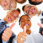 A group of smiling diverse professionals leaning in and giving a thumbs up to the camera.